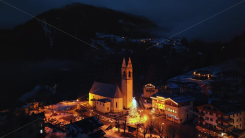 Selva di Cadore, Italy – January 11, 2025: Aerial drone view of the San Lorenzo Church illuminated at night in the Selva di Cadore comune in Dolomites, Italy - Starpik Stock