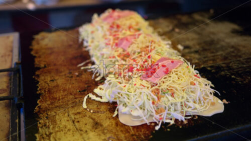 Close up of Okonomiyaki, Japanese cabbage pancakes being cooked at a street food market in Japan - Starpik Stock