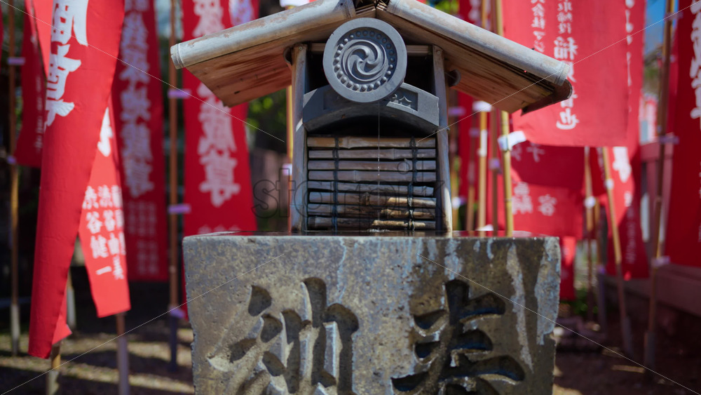 Close up of a small water fountain surrounded by red flags at the Senso-ji temple in Asakusa, Tokyo, Japan - Starpik Stock