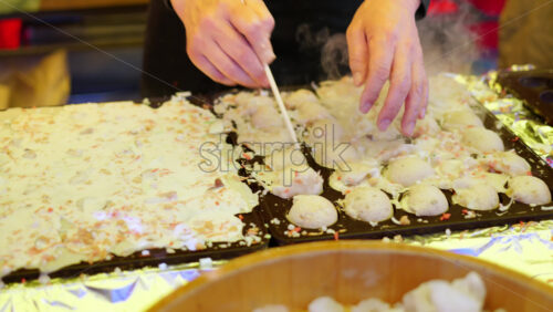 Close up of squid dumplings being cooked on a cast iron takoyaki grill pan at a street food market in Japan - Starpik Stock