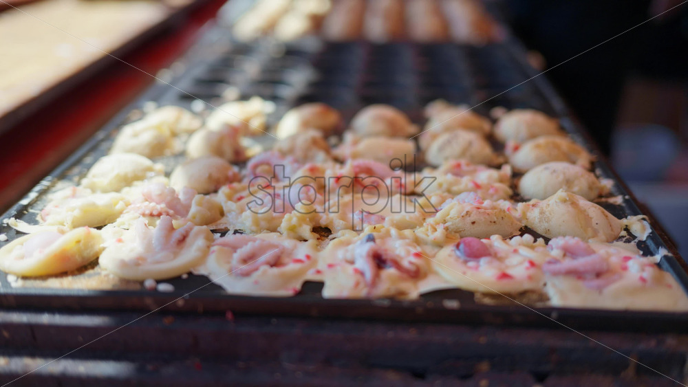 Close up of squid dumplings being cooked on a cast iron takoyaki grill pan at a street food market in Japan - Starpik Stock