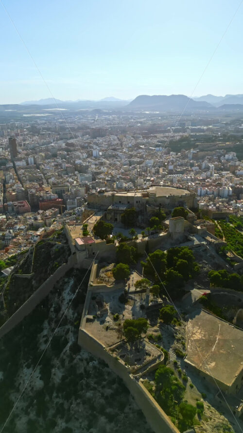 Aerial drone view of the Santa Barbara Castle on the coast of Alicante, Spain with the city and the sea on the background. Vertical - Starpik Stock