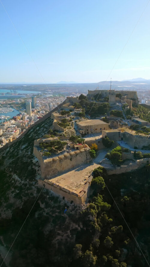 Aerial drone view of the Santa Barbara Castle on the coast of Alicante, Spain with the city and the sea on the background. Vertical - Starpik Stock
