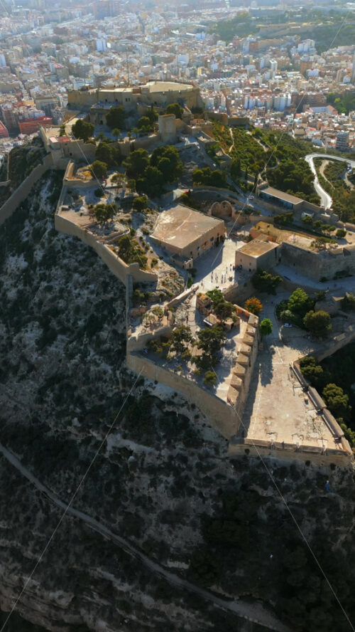 Aerial drone view of the Santa Barbara Castle on the coast of Alicante, Spain with the city on the background. Vertical - Starpik Stock