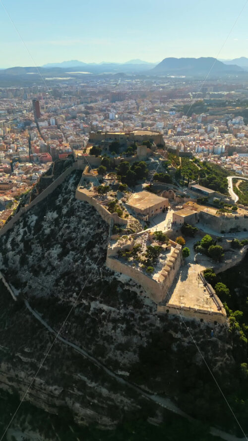 Aerial drone view of the Santa Barbara Castle on the coast of Alicante, Spain with the city on the background. Vertical - Starpik Stock