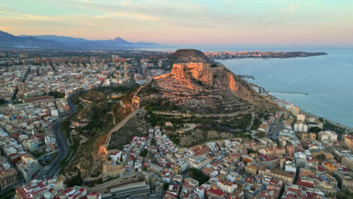 Aerial drone view of the Santa Barbara Castle surrounded by buildings on the coast of Alicante, Spain with the sea on the background - Starpik Stock