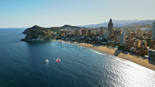 Aerial drone view of the buildings along the coastline with people parasailing in the sea in Benidorm, Spain in daylight - Starpik Stock