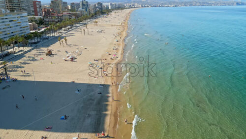 Aerial drone view of the buildings along the coastline with people relaxing on the beach in Alicante, Spain in daylight - Starpik Stock
