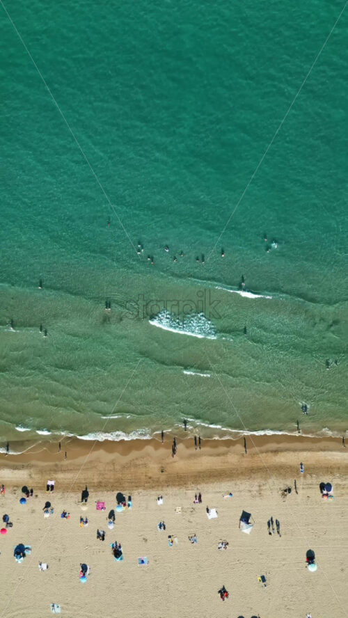 Aerial drone view of the buildings along the coastline with people relaxing on the beach in Alicante, Spain in daylight. Vertical - Starpik Stock