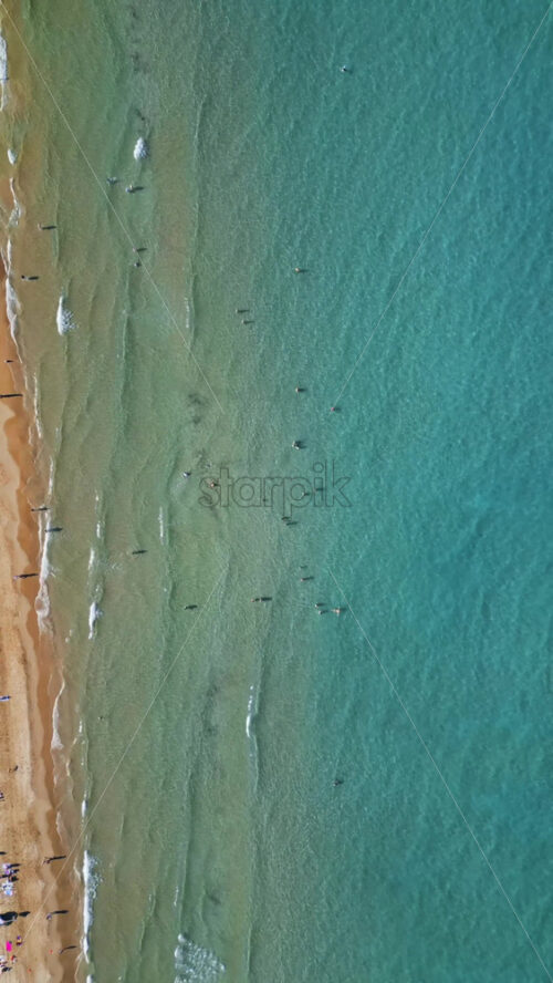 Aerial drone view of the buildings along the coastline with people relaxing on the beach in Alicante, Spain in daylight. Vertical - Starpik Stock