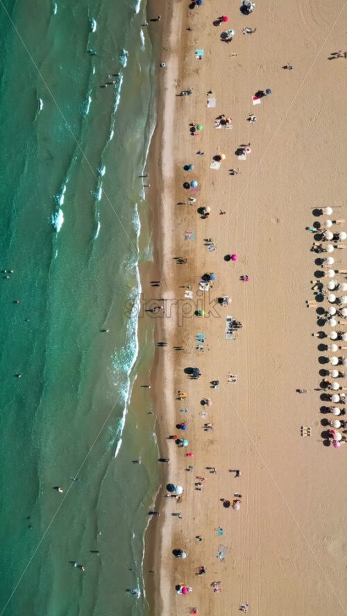 Aerial drone view of the buildings along the coastline with people relaxing on the beach in Alicante, Spain in daylight. Vertical - Starpik Stock