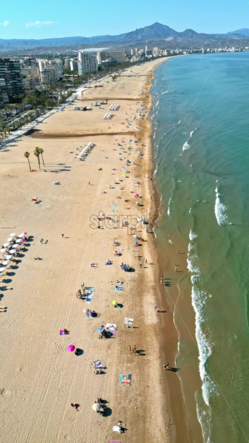 Aerial drone view of the buildings along the coastline with people relaxing on the beach in Alicante, Spain in daylight. Vertical - Starpik Stock