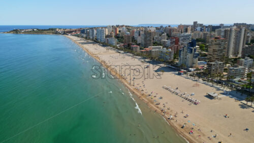 Aerial drone view of the buildings along the coastline with people relaxing on the beach in Benidorm, Spain in daylight - Starpik Stock