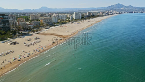 Aerial drone view of the buildings along the coastline with people relaxing on the beach in Benidorm, Spain in daylight - Starpik Stock
