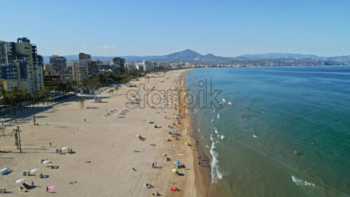 Aerial drone view of the buildings along the coastline with people relaxing on the beach in Benidorm, Spain in daylight - Starpik Stock