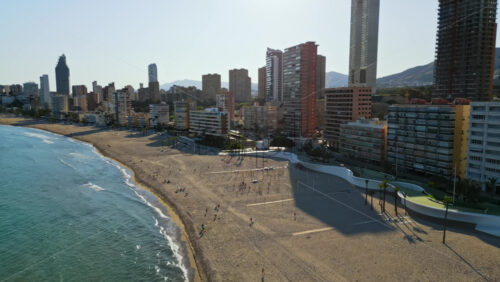 Aerial drone view of the buildings along the coastline with people relaxing on the beach in Benidorm, Spain in daylight - Starpik Stock