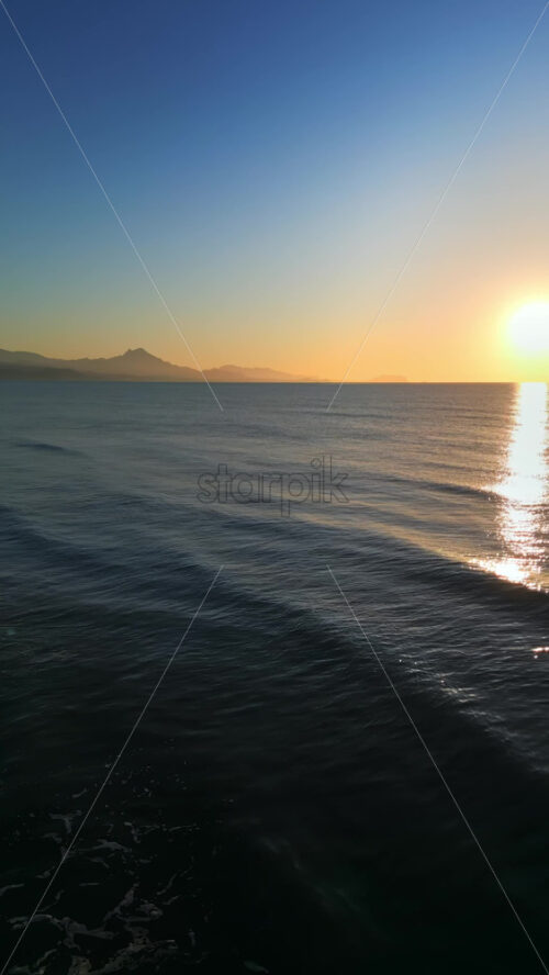 Aerial drone view of waves hitting the shore on the beach in Alicante, Spain at sunset. Vertical - Starpik Stock
