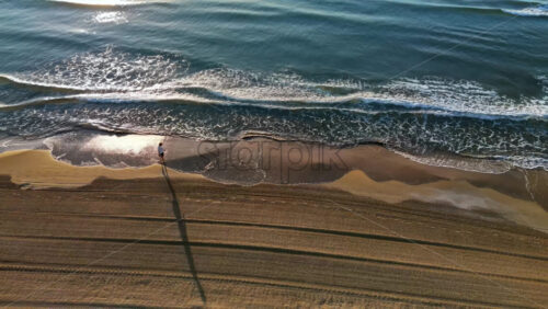 Man walking on the beach with waves hitting the shore in Alicante, Spain - Starpik Stock