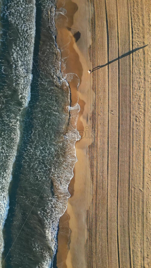 Man walking on the beach with waves hitting the shore in Alicante, Spain. Vertical - Starpik Stock