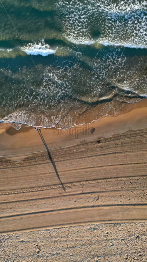Man walking on the beach with waves hitting the shore in Alicante, Spain. Vertical - Starpik Stock