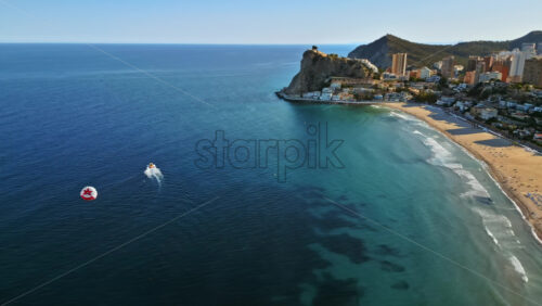 Video – Aerial drone view of the buildings along the coastline with people parasailing in the sea in Benidorm, Spain in daylight - Starpik Stock