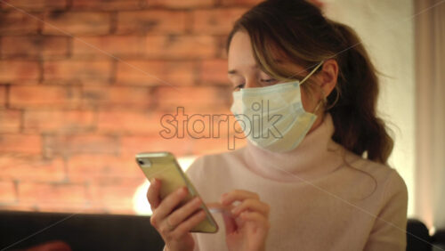 Video - Brunette woman wearing a mask scrolling on her phone at a restaurant