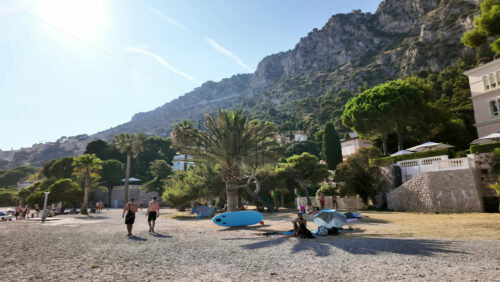 Video - Beaulieu-sur-Mer, France - July 5, 2024: People walking on the beach and relaxing in the sea at the Petite Afrique Beach