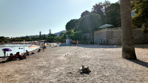 Video - Beaulieu-sur-Mer, France - July 5, 2024: People walking on the beach and relaxing in the sea at the Petite Afrique Beach