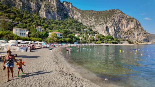 Video - Beaulieu-sur-Mer, France - July 5, 2024: People walking on the beach and relaxing in the sea at the Petite Afrique Beach