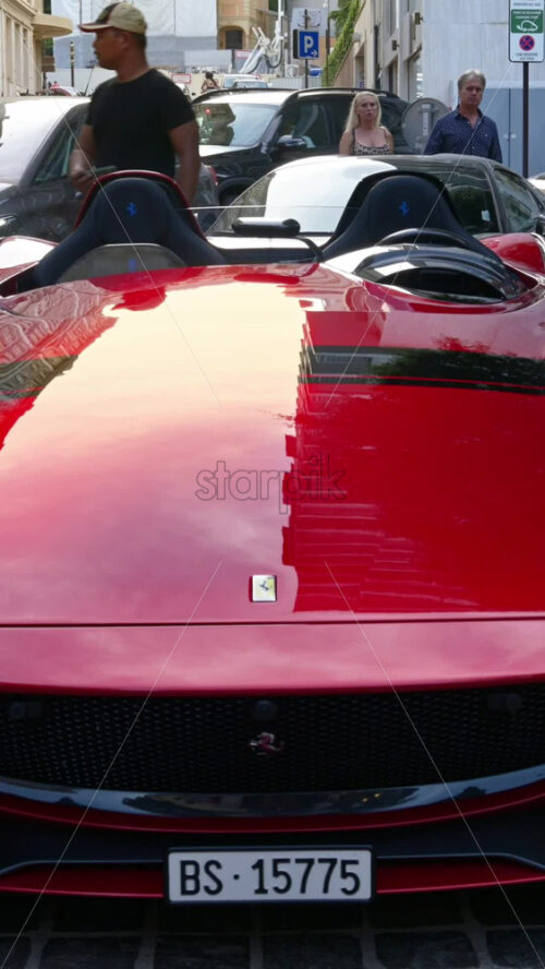 Video - Monte Carlo, Monaco - October 4, 2024 : Red Ferrari parked on the street with people walking around. Vertical