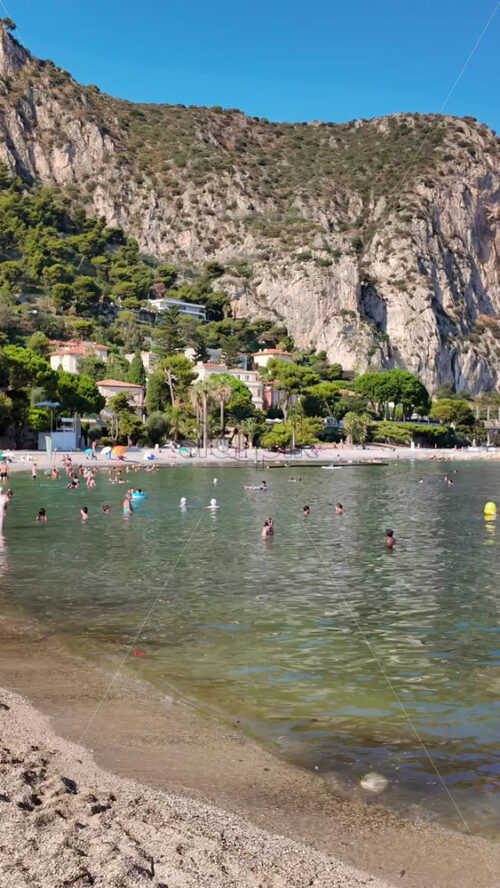 Video - Beaulieu-sur-Mer, France - July 5, 2024: People walking on the beach and relaxing in the sea at the Petite Afrique Beach. Vertical