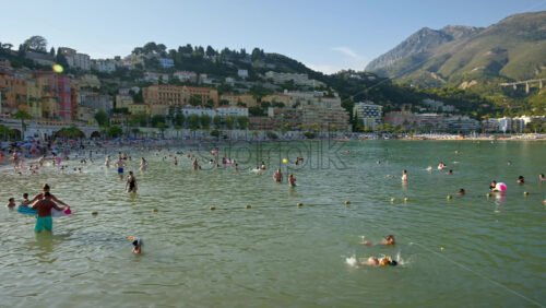 Video - Menton, France - September 4, 2024: People swimming in the sea with a view of the colourful buildings in the city