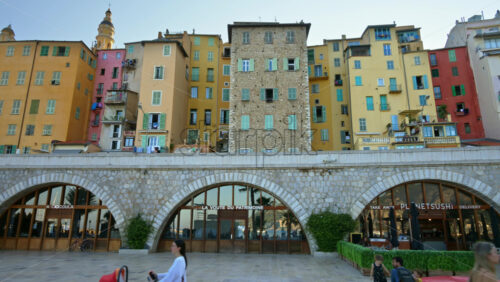 Video - Menton, France - September 4, 2024: View of the colourful buildings in the city and people walking by the coastline