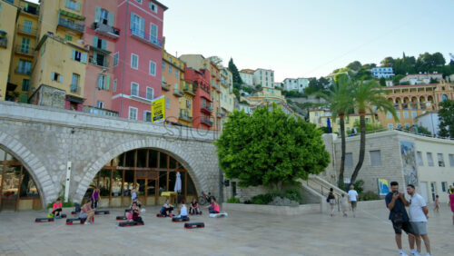 Video - Menton, France - September 4, 2024: View of the colourful buildings in the city and people walking by the coastline