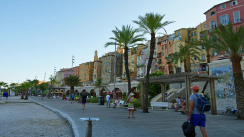 Video - Menton, France - September 4, 2024: View of the colourful buildings in the city and people walking by the coastline