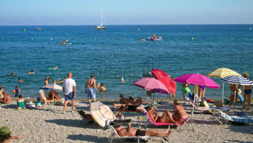 Video - Menton, France - September 4, 2024: People swimming and relaxing on the beach under sun umbrellas