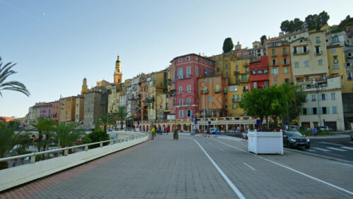 Video - Menton, France - September 4, 2024: View of the colourful buildings in the city and people walking by the coastline