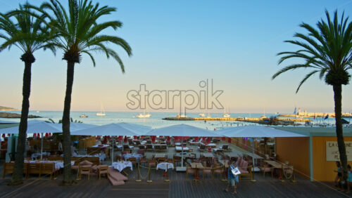 Video - Menton, France - September 4, 2024: Palm trees near a restaurant on the beach