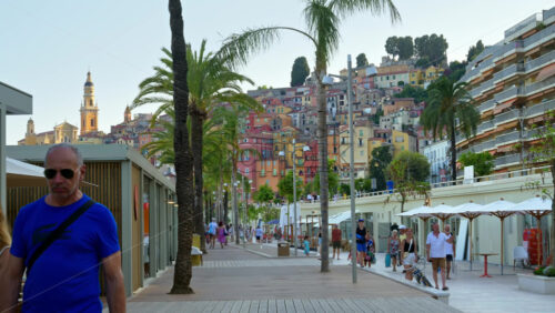 Video - Menton, France - September 4, 2024: View of the colourful buildings in the city and people walking by the coastline