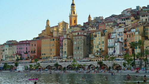 Video - Menton, France - September 4, 2024: People swimming in the sea with a view of the colourful buildings in the city