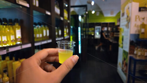 Video - Close up of a woman's hand holding a shot of limoncello in a store