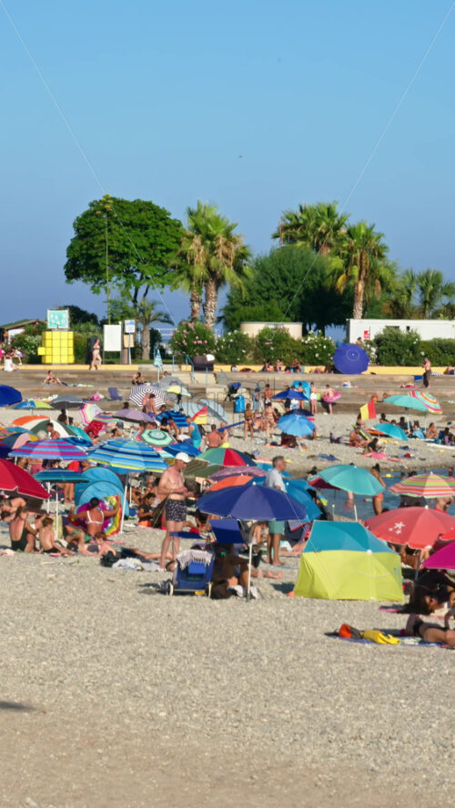 Video - Menton, France - September 4, 2024: People swimming and relaxing on the beach under sun umbrellas. Vertical