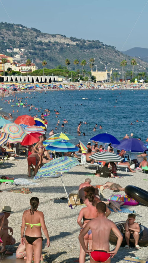 Video - Menton, France - September 4, 2024: People swimming and relaxing on the beach under sun umbrellas. Vertical