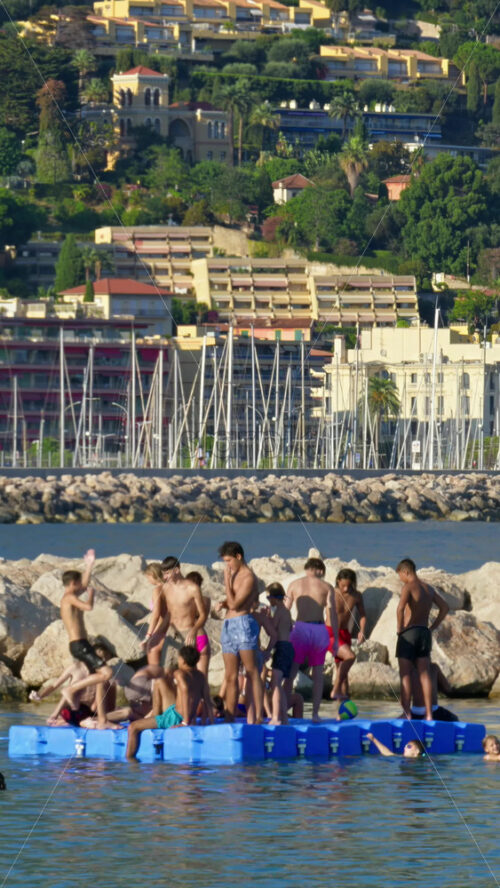 Video - Menton, France - September 4, 2024: People swimming in the sea with a view of the colourful buildings in the city. Vertical