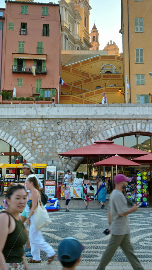 Video - Menton, France - September 4, 2024: View of the colourful buildings in the city and people walking by the coastline. Vertical