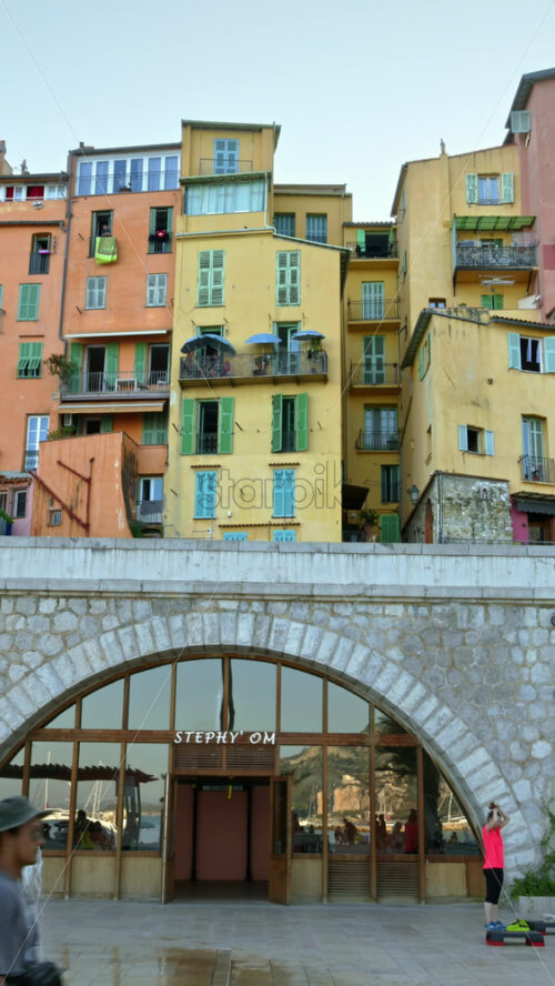Video - Menton, France - September 4, 2024: View of the colourful buildings in the city and people walking by the coastline. Vertical