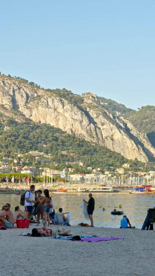 Video - Menton, France - September 4, 2024: People swimming and relaxing on the beach. Vertical