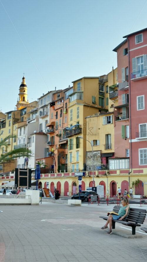 Video - Menton, France - September 4, 2024: View of the colourful buildings in the city and people walking by the coastline. Vertical