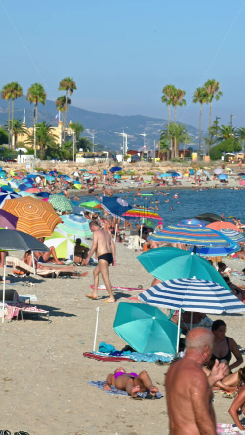 Video - Menton, France - September 4, 2024: People swimming and relaxing on the beach under sun umbrellas. Vertical