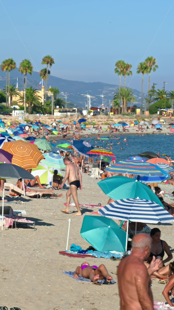 Video - Menton, France - September 4, 2024: People swimming and relaxing on the beach under sun umbrellas. Vertical